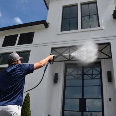 A man using a pressure washer to clean the house of a modern white house.